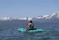 Kayaker on the crystal blue waters of Lake Tahoe.  Mountians rise above the lake in the distance.